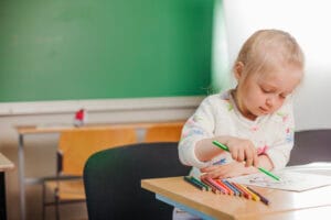 Young girl sitting and drawing to develop fine motor skills for kindergarten readiness