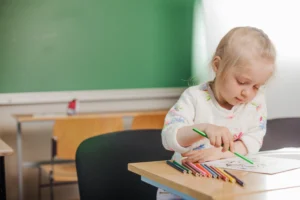 Young girl sitting and drawing to develop fine motor skills for kindergarten readiness