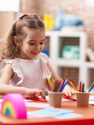 Adorable caucasian girl sitting on table drawing on paper at classroom