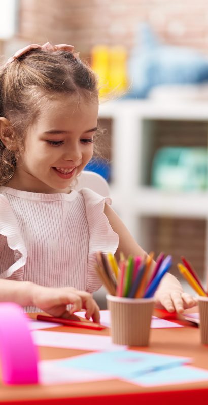 Adorable caucasian girl sitting on table drawing on paper at classroom
