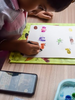 Smart Indian little boy perform thumb painting with different colourful water colour kit during the summer vacations, Cute Indian Kid doing colourful thumb painting drawing on wooden table