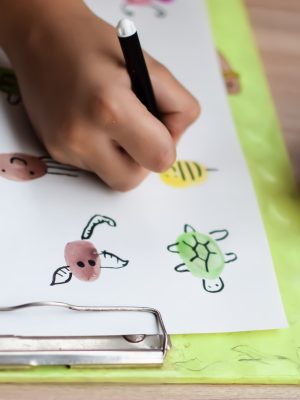Smart Indian little boy perform thumb painting with different colourful water colour kit during the summer vacations, Cute Indian Kid doing colourful thumb painting drawing on wooden table